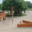 Nature Ship Sandbox, wooden playhouse dans une aire de jeux sablonneuse avec des arbres autour.