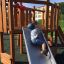Enfant jouant sur le toboggan Nature Ship Sandbox, wooden playhouse.