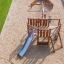Maisonnette de jeu en bois Nature Ship Sandbox avec toboggan dans une aire de jeux.