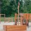 Structure extérieure de maisonnette en bois avec Nature Ship Sandbox dans un cadre d’aire de jeux.