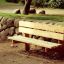 Larchwood Bench placé dans un parc à côté d’un mur en pierre.