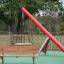 Larchwood Bench dans une aire de jeux avec une balançoire et un toboggan en arrière-plan'