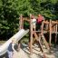 Enfants jouant sur un ensemble de jeux en bois Alstad avec un toboggan et une structure d’escalade.
