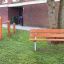 Banc en structure acier dans un parc avec du matériel de fitness en bois à l'arrière-plan.