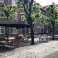 Tables et bancs ensemble Quadro sous des parasols dans une rue pavée bordée d’arbres.