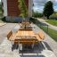Ensemble extérieur en bois Table & Bench Quadro sur une zone pavée avec de la verdure en arrière-plan
