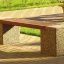 Banc de parc extérieur Vega avec lattes en bois et supports en béton sur une allée pavée de briques.