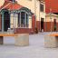 Banc en béton Vega dans une cour avec des bâtiments historiques en arrière-plan.