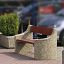 Banc extérieur Dona avec assise en bois rouge et côtés en béton placé entre deux bacs à plantes.