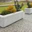 Jardinières en béton Milano avec des plantes sur une surface pavée.