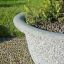 Grande jardinière en pierre Bell remplie de plantes sur un chemin de galets.