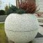 Bac à plantes de jardin en pierre 'Globe' avec des plantes éclatantes devant une maison.