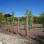 Équipement de terrain de jeu extérieur Triple Somersault Nature dans un jardin avec des arbres et un ciel dégagé.