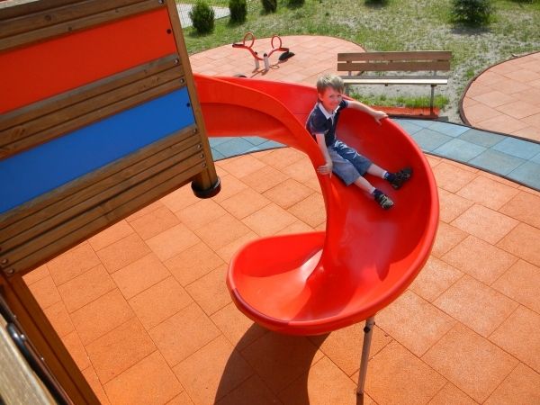 Enfant jouant sur un toboggan spiral rouge sur Rubber Tiles 90