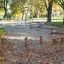 Aire de jeux extérieure avec la poutre d’équilibre Cape Code et des rondins de marche parmi les arbres dans un parc.