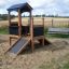 Playhouse Nature dans une aire de jeux sablonneuse avec un banc en arrière-plan.