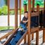 Enfant jouant sur Knight's Castle Nature playhouse with slide.