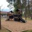 Knight's Castle Nature playhouse with slide dans une aire de jeux boisée.