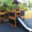 Tower Nature wooden playhouse with slide dans une aire de jeux.