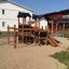 Tower Nature wooden playhouse with slide sur une aire de jeux sablonneuse.