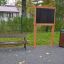 Banc de parc, tableau noir et poubelle installés dans une zone de parc.