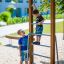 Des enfants jouent sur une échelle verticale en bois dans une aire de jeux.