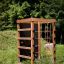 Cabane de jeu en bois avec boîte d’escalade dans un espace extérieur herbeux.