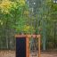 Cabane de jeu en bois avec mur d’escalade dans une aire de jeux forestière.