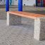 Banc extérieur en bois et en béton Wika devant un bâtiment.