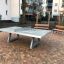 Concrete table tennis, free-standing sur une cour pavée avec des bancs en arrière-plan