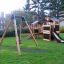 Balançoire en bois Swing Frame (single swing) dans une aire de jeux avec structure d'escalade et toboggan.