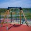 Swing Frame (single swing, wide) avec des poteaux en bois et un siège de balançoire circulaire dans une aire de jeux