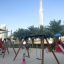 Swing Frame (single swing, wide) dans une aire de jeux ensoleillée avec des enfants qui jouent.