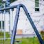 Swing Metal Frame (single swing, wide) en extérieur avec un bâtiment blanc flou en arrière-plan.