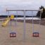 Swing Metal Frame (double swing) dans une aire de jeux avec un toboggan jaune en arrière-plan.