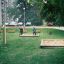 Swing seat: Flexi seat dans un parc verdoyant avec des bacs à sable et des enfants qui jouent