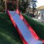 Slide rouge et argenté sur une colline herbeuse dans une aire de jeux