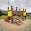 Aire de jeux pour enfants Mini play avec toboggan, escaliers et base en sable dans un parc extérieur.