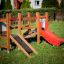 Mini play ensemble de jeux en bois avec un toboggan rouge et une rampe d’escalade sur une pelouse verte.
