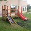 Structure en bois Mini play avec toboggan rouge et rampe d’escalade dans une aire de jeux de jardin