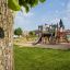 Aire de jeux Camelot castle with slide dans un parc verdoyant.