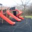 Équipement de aire de jeux rouge avec trois toboggans, dont un toboggan en spirale.