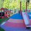 Aire de jeux extérieure avec Hill Slide SL120 présentant un monticule coloré et un toboggan rouge.
