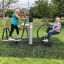 Deux seniors utilisant des équipements de gym en plein air Set 8 sur une zone herbeuse d’un parc.