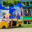 Enfant jouant dans un véhicule de aire de jeux jaune Taxi près d’un train de jeu vert.