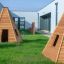 Wigwam wooden house sur de l’herbe verte près de bâtiments modernes