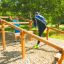 Enfants jouant sur Climb Obstacle wooden ladder dans une aire de jeux extérieure.