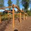 Échelle d’obstacles d’escalade en bois dans une aire de jeu extérieure entourée d’arbres.