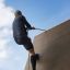 Homme grimpant sur le Climbing Ramp steel structure à l’aide d’une corde.