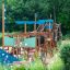 Structure de terrain de jeu en bois Majestic ship with slide avec des accents bleus dans un parc verdoyant.